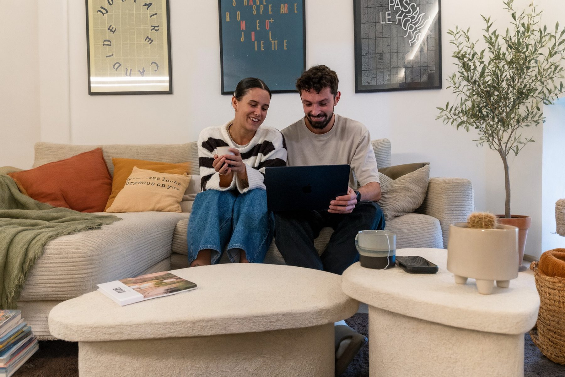 Le même couple, souriant, regarde l'ordinateur ensemble : la table est rangée, il reste une tasse et un magazine