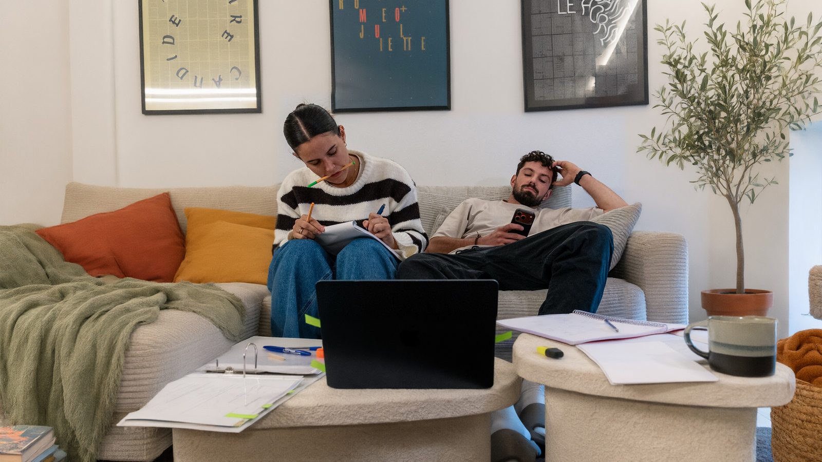 Un couple sur son canapé : elle prend des notes au milieu des devis et du classeur, lui décroche sur son téléphone