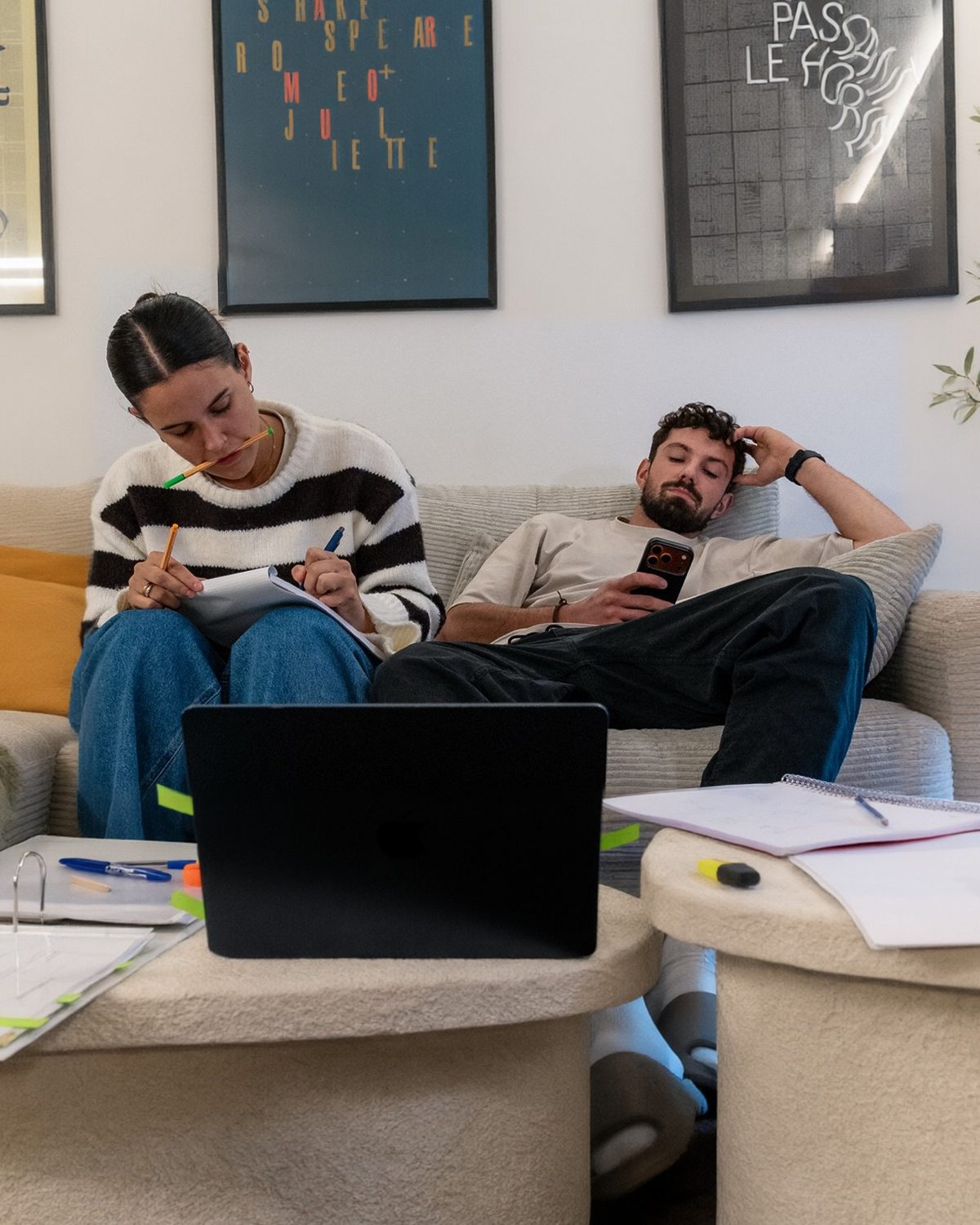 Un couple sur son canapé : elle prend des notes au milieu des devis et du classeur, lui décroche sur son téléphone
